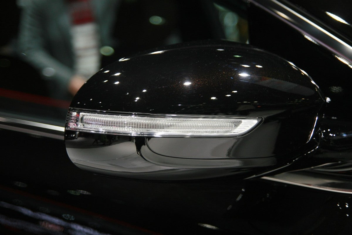 Car side view mirror with glass lens, mirror housing, indicator light, mirror cover, adjustment motor, base mount, wiring harness, folding mechanism, and blind spot detection sensor on a modern vehicle